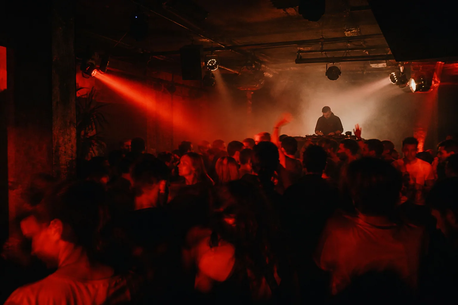 Publika i DJ u intimnom klubu pod crvenim svjetlom i toplom izmaglicom.